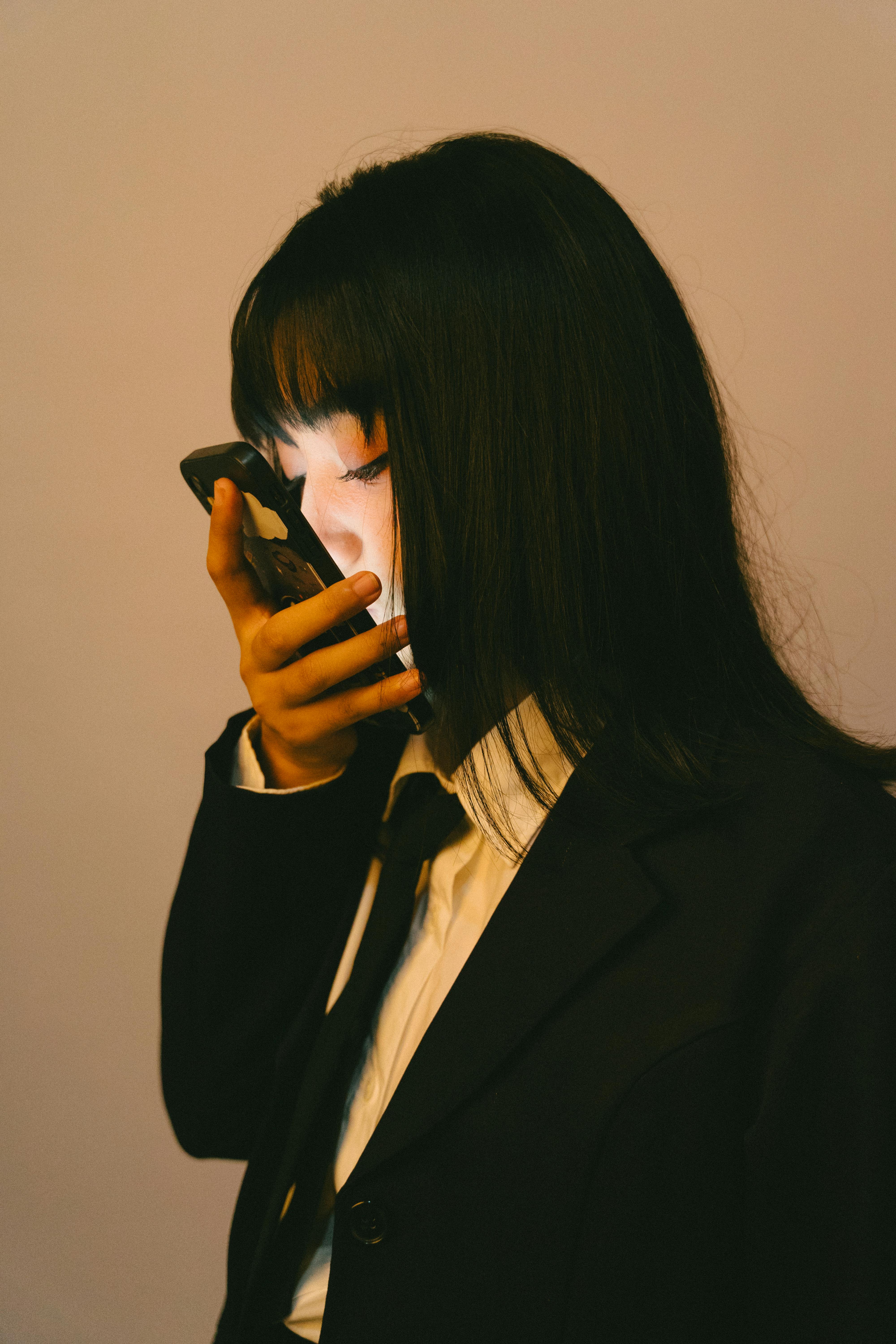 Bezpłatne Młoda, profesjonalna kobieta w garniturze sprawdza smartfon w warunkach słabego oświetlenia, tworząc intrygującą atmosferę. Zdjęcie z galerii