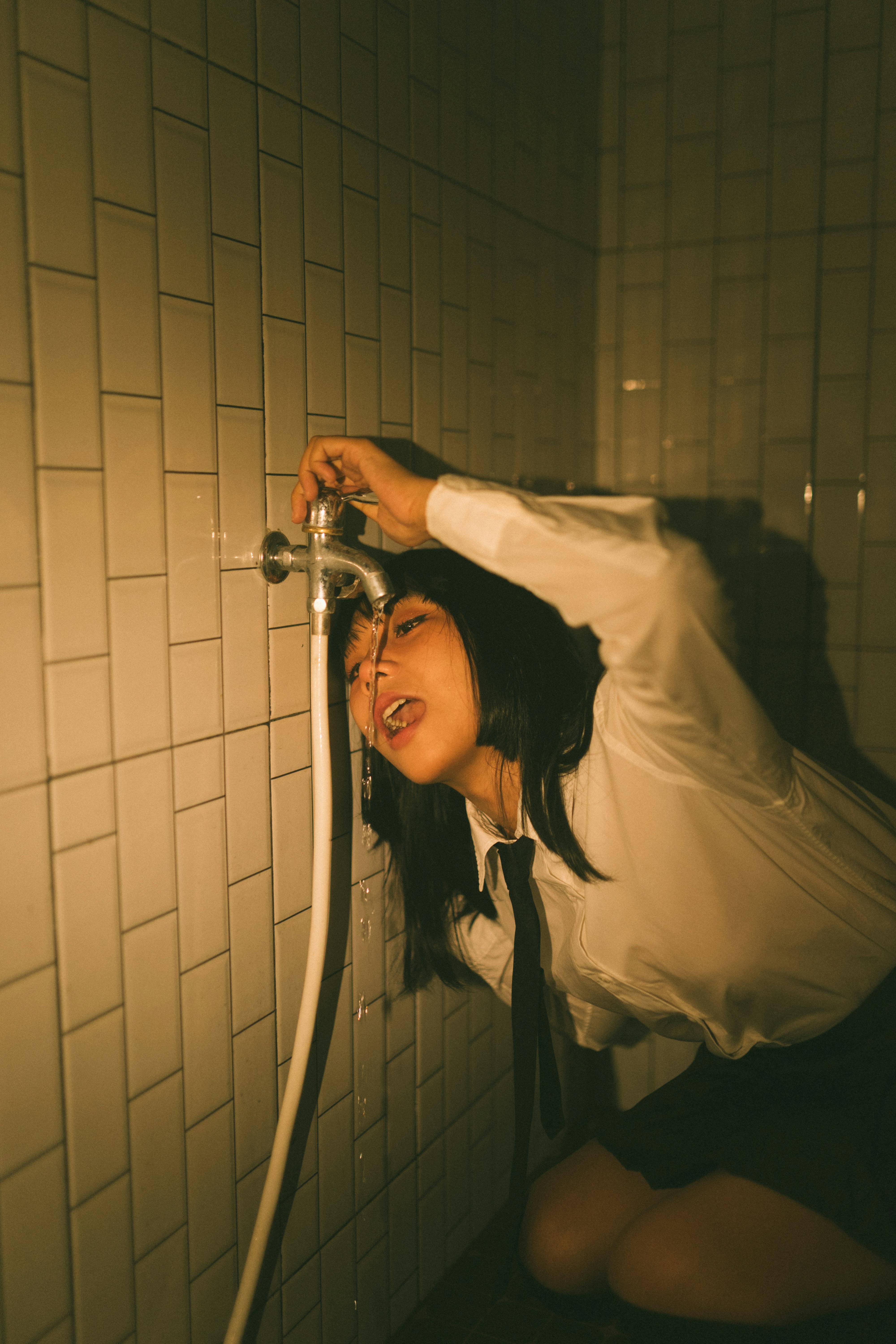 Ücretsiz Loş ışıklı, fayans kaplı bir odada musluk kullanan bir yetişkinin sanatsal görüntüsü. Stok Fotoğraflar