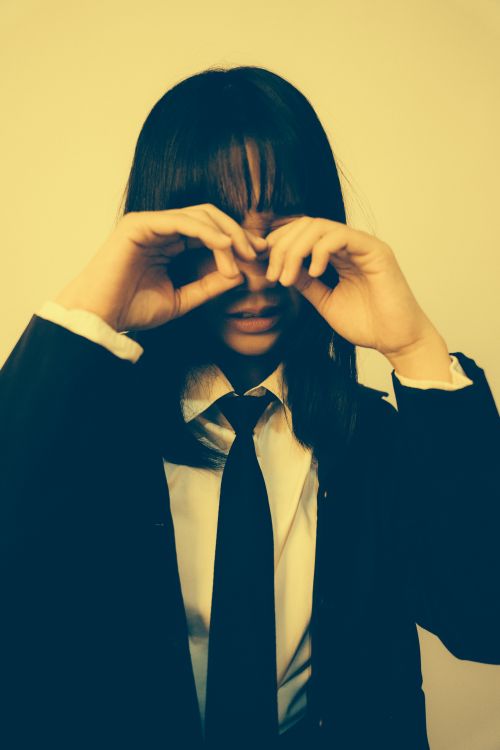 Free Artistic sepia portrait of a young woman playfully covering her eyes, creating a mysterious mood. Stock Photo
