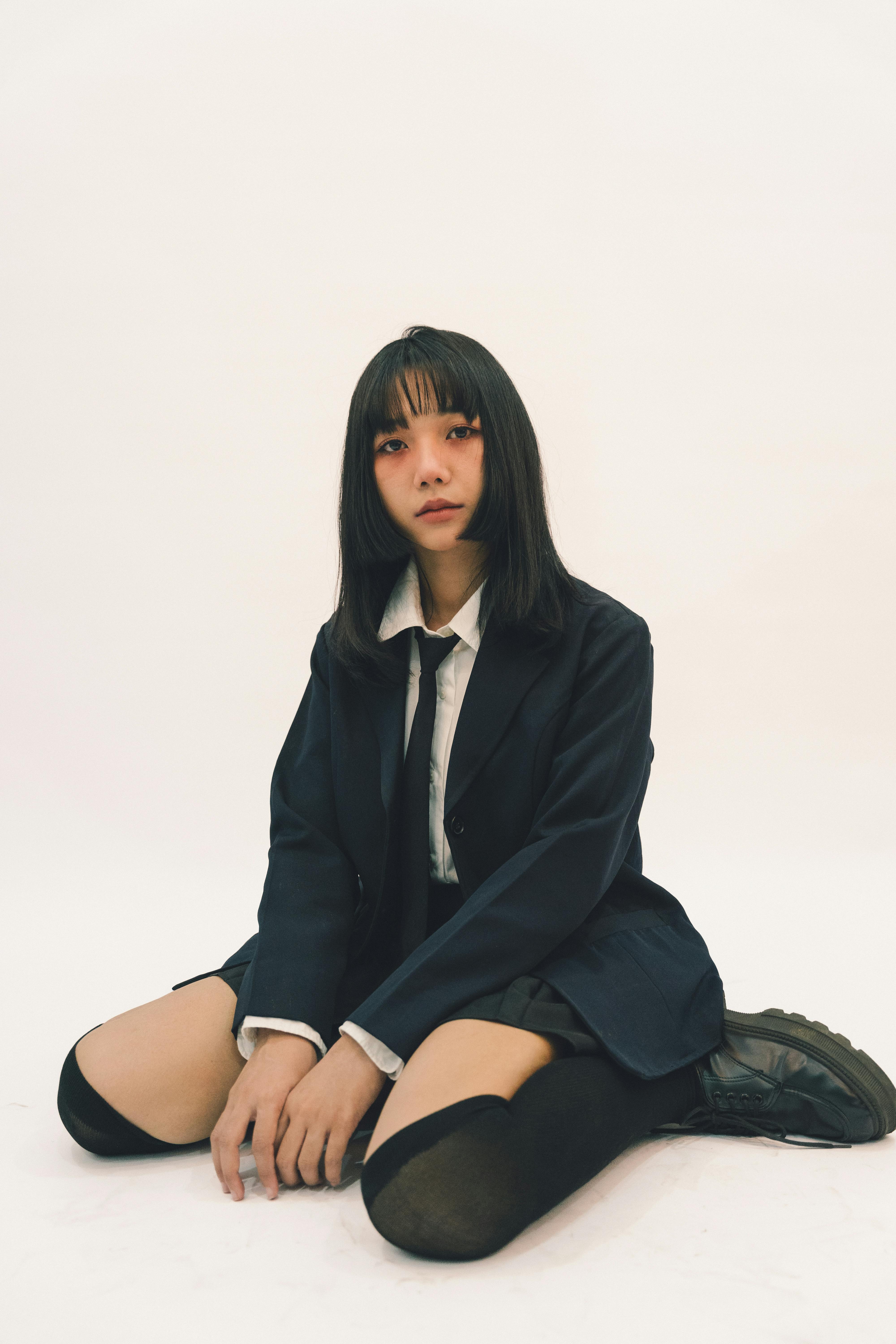 Ücretsiz Okul üniforması giymiş, şık giyimli genç bir yetişkinin nötr bir arka plan önünde oturduğu portre. Stok Fotoğraflar