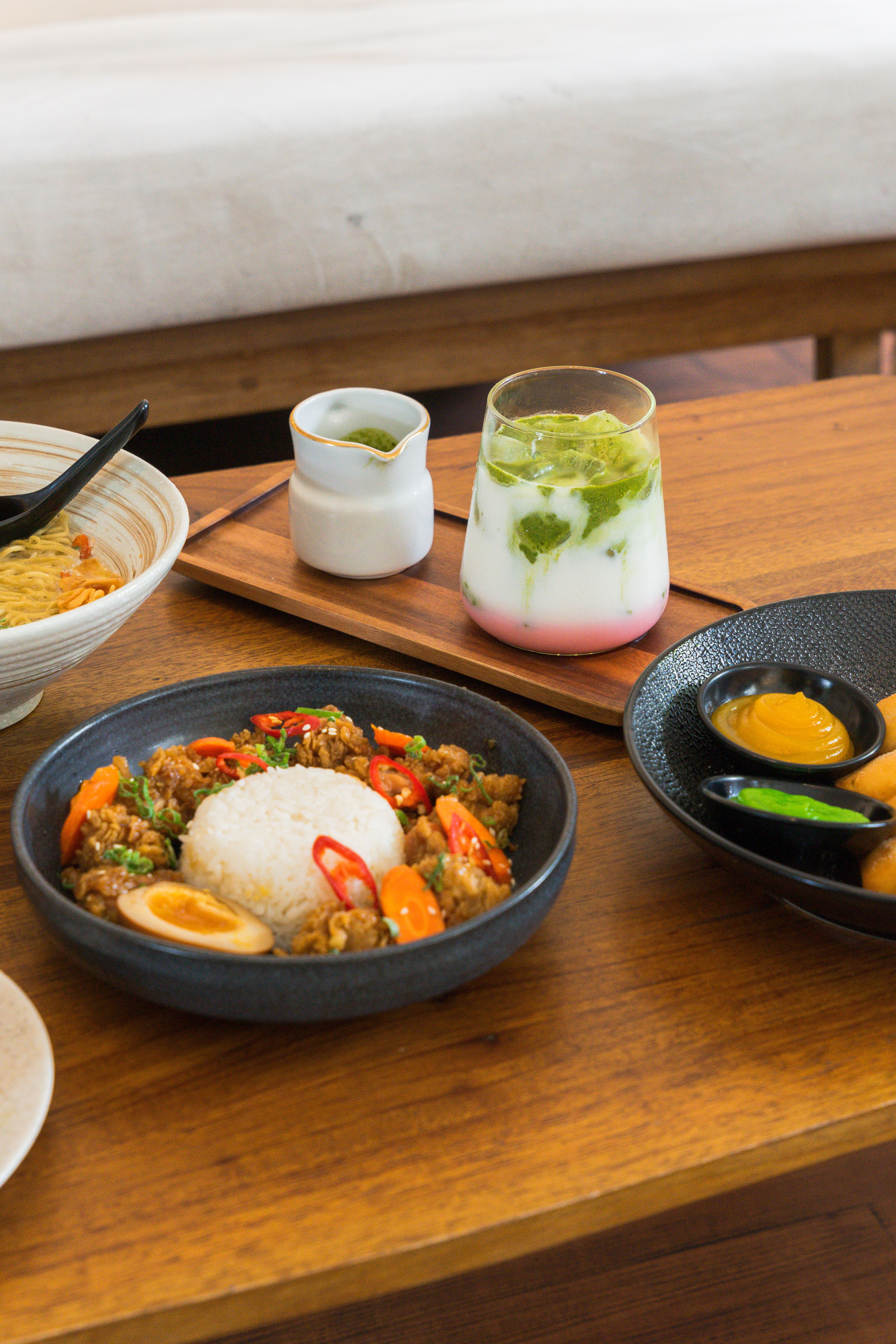 Colorful Asian dishes with rice, noodles, and a refreshing drink on a wooden table.