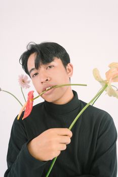 A young man in a black turtleneck poses with vibrant flowers against a minimalist backdrop. - Fotografer Sidoarjo