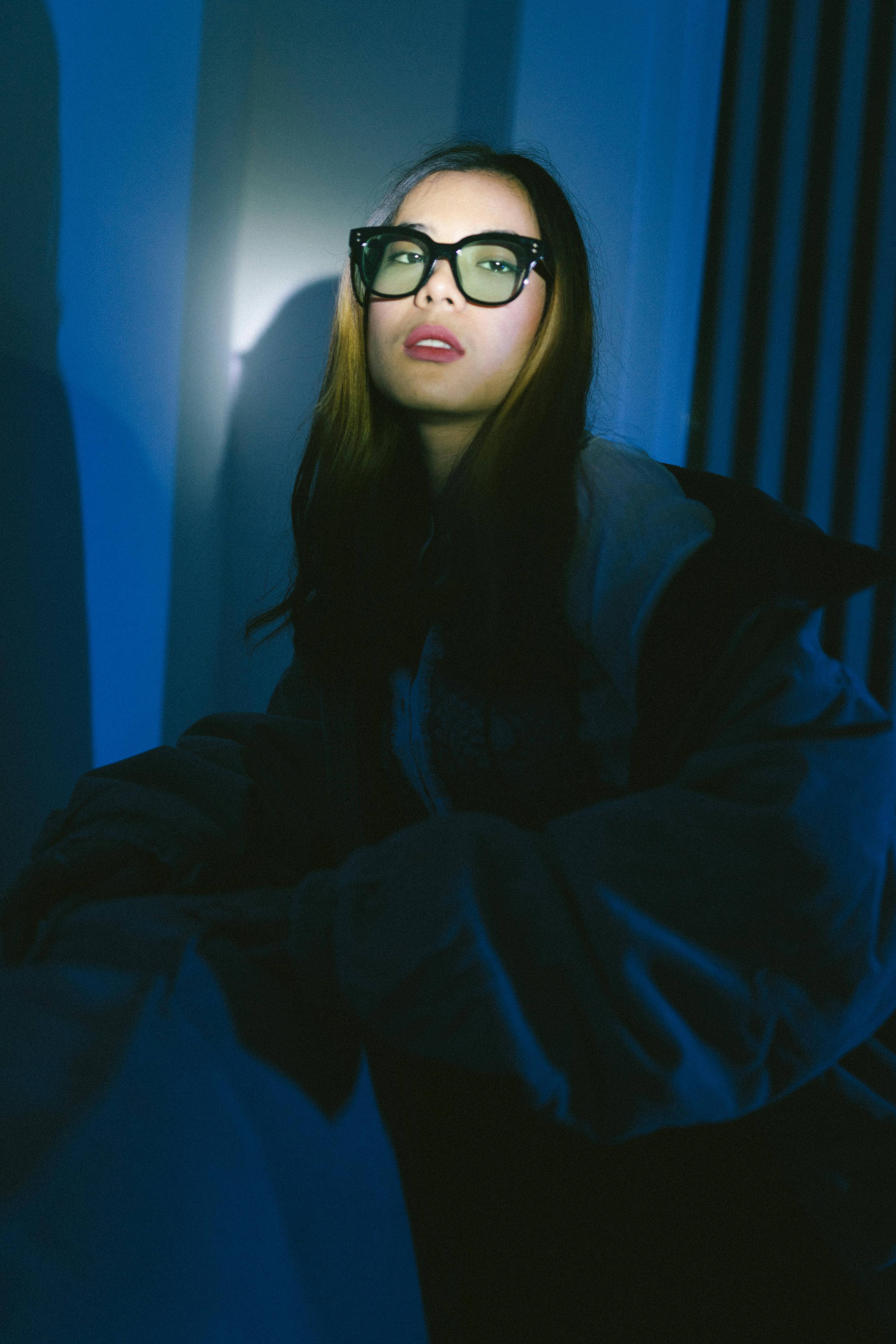 Kostenlos Künstlerisches Porträt einer Frau mit Brille in dramatischem blauem Licht, das eine geheimnisvolle Aura ausstrahlt. Stock-Foto