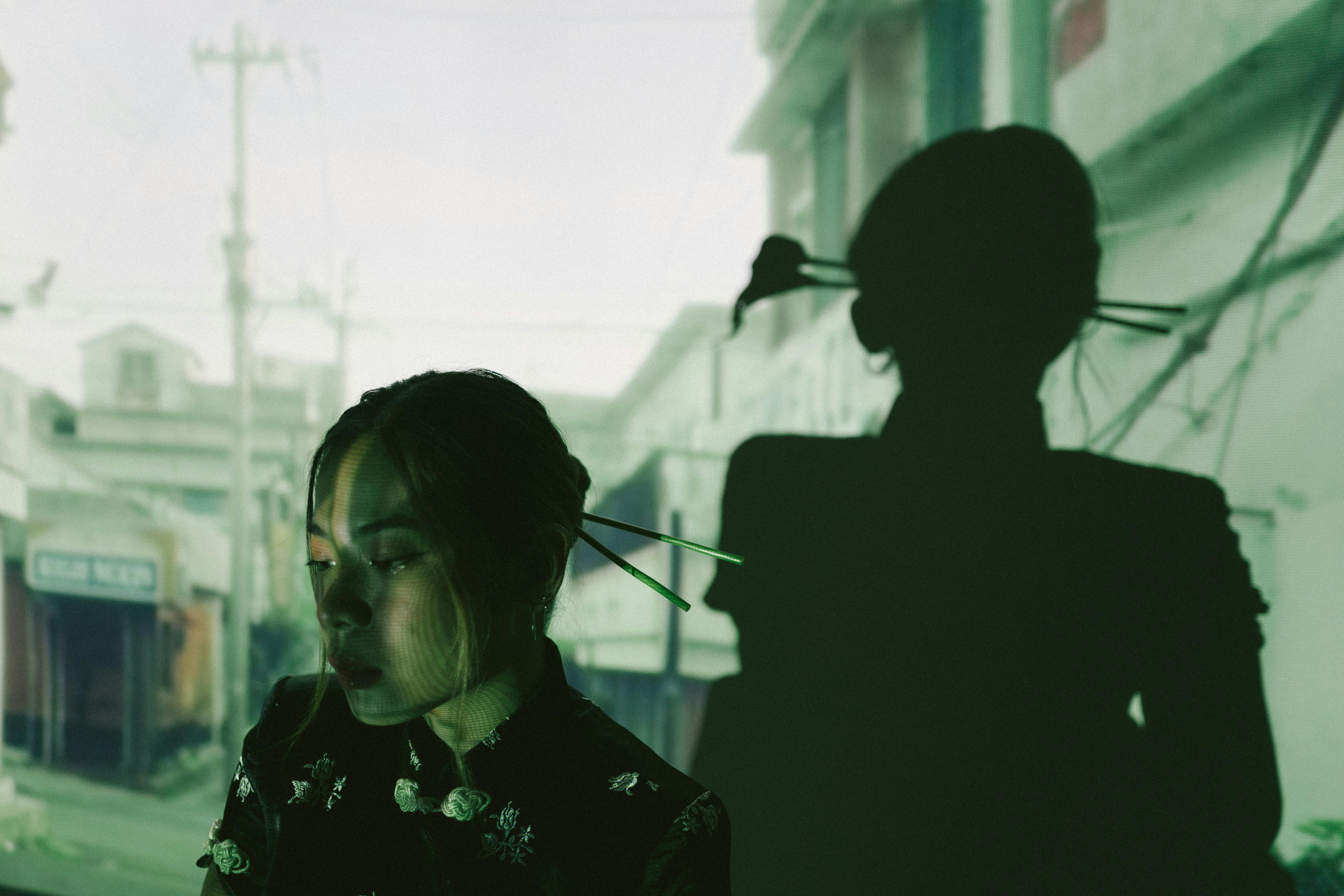Free Artistic portrait of a pensive woman with shadowed silhouette in an urban street setting. Stock Photo