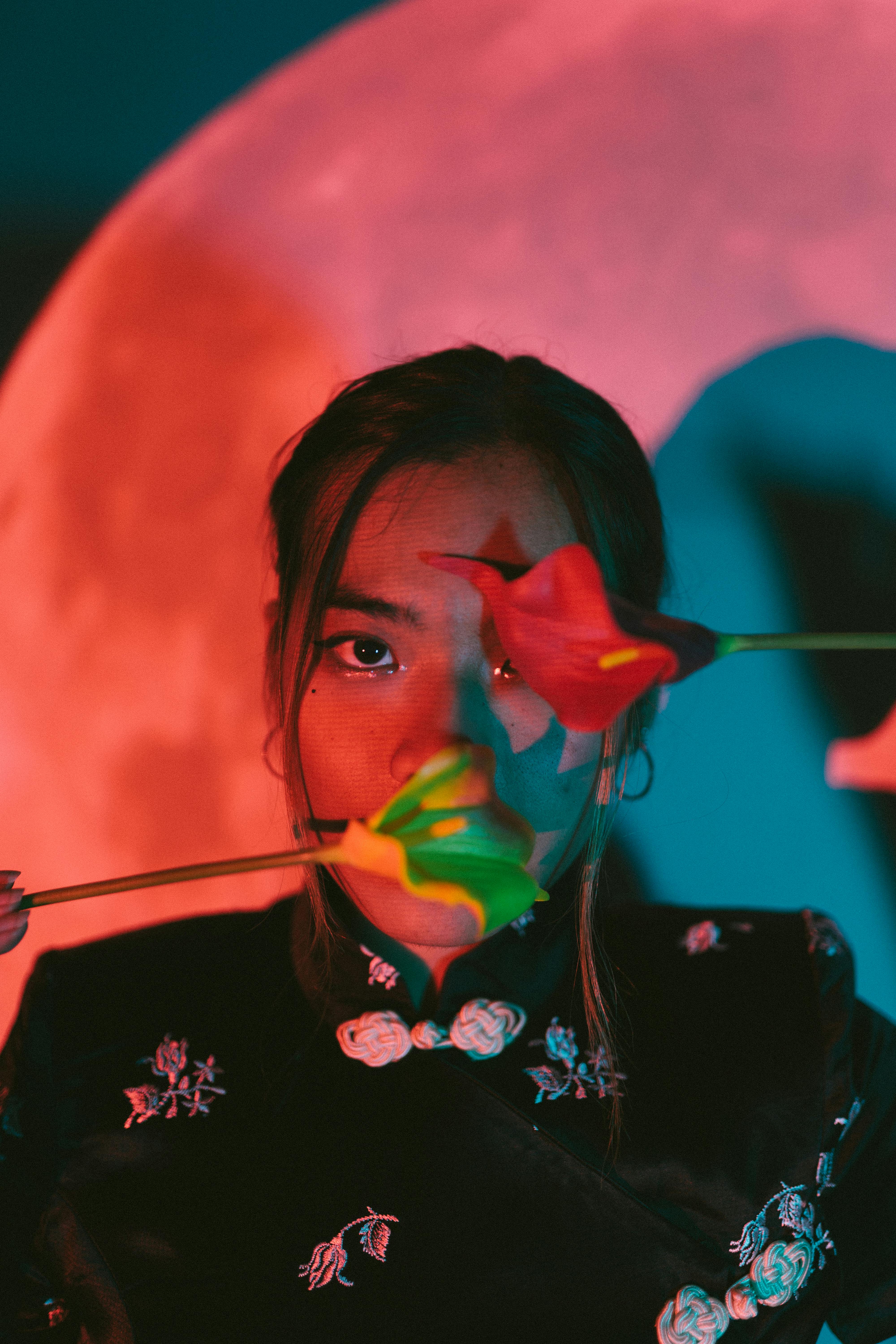 bezplatná Umělecký portrét ženy schované za zářivými květinami na barevném abstraktním pozadí. Základová fotografie