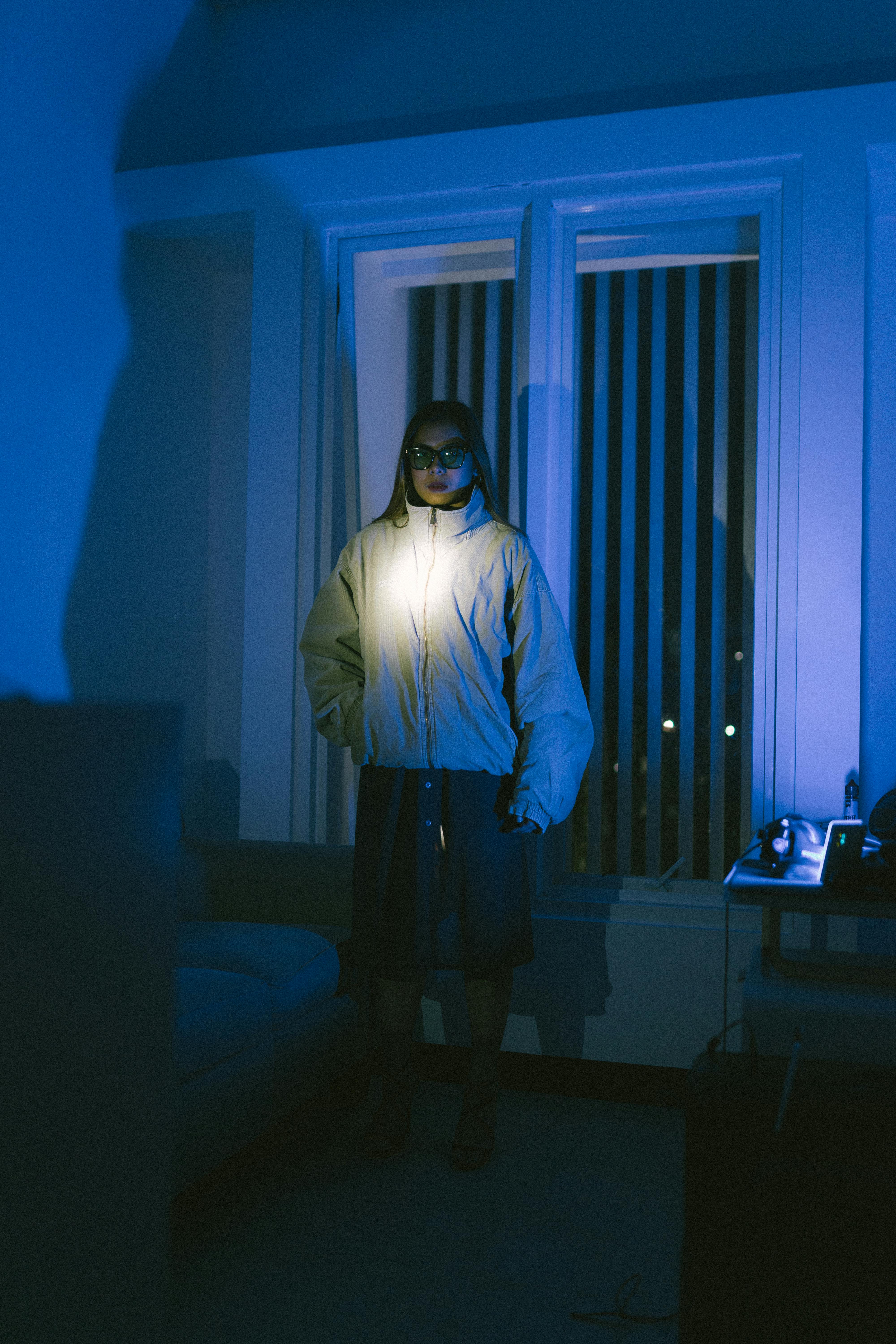 Free A person with sunglasses stands in a dimly lit room, illuminated by a flashlight. Stock Photo