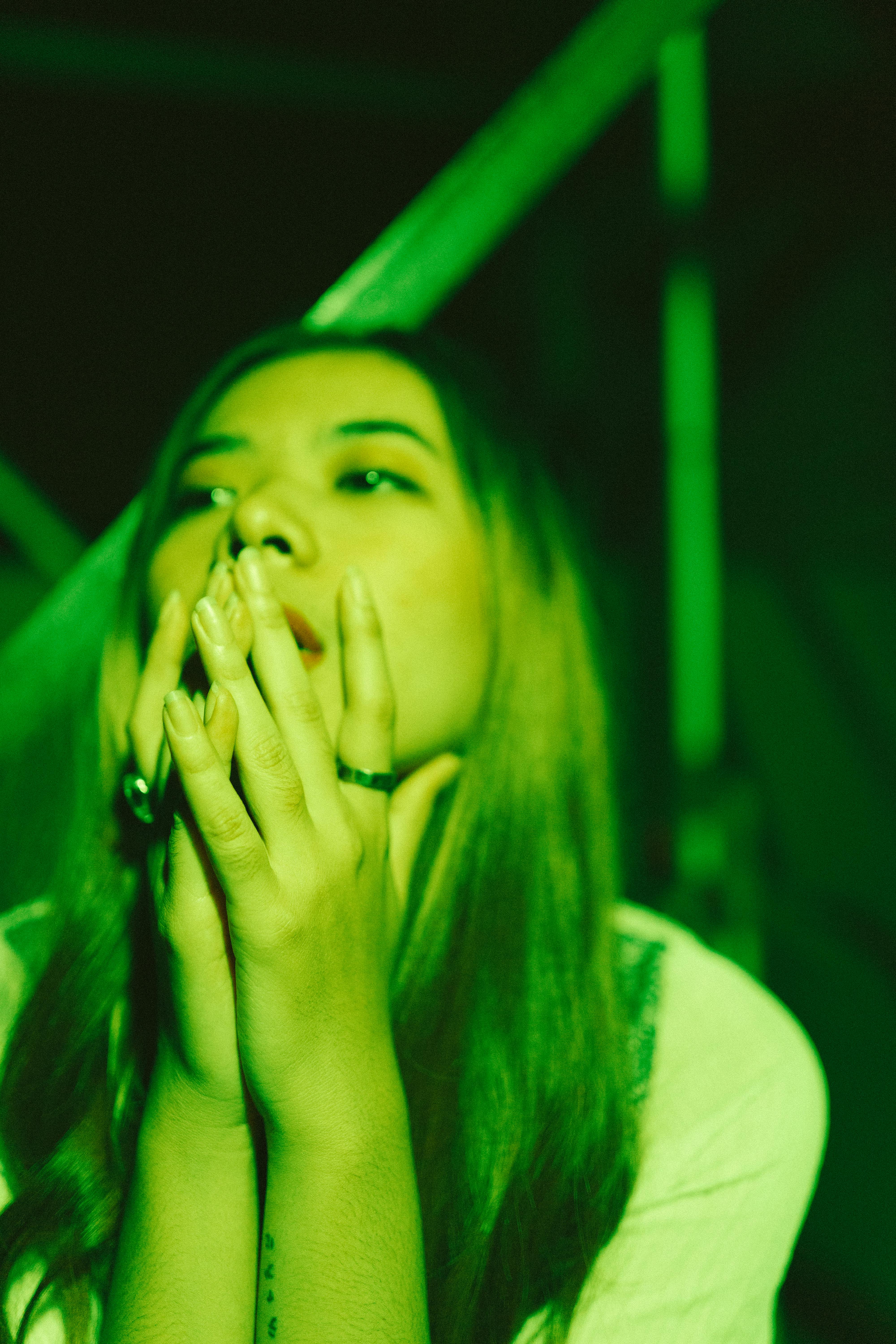 Gratuit Femeie gânditoare, cu mâinile împreunate, scăldată în lumină verde noaptea. Fotografie de stoc