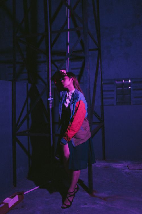 Free A woman stands in a dimly lit industrial space, casting soft shadows under purple lighting. Stock Photo