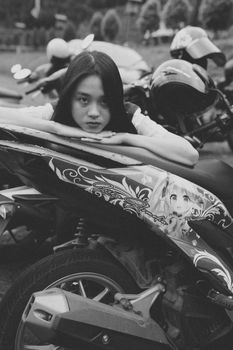 Black and white photo of a young woman leaning on a motorcycle with anime art.
