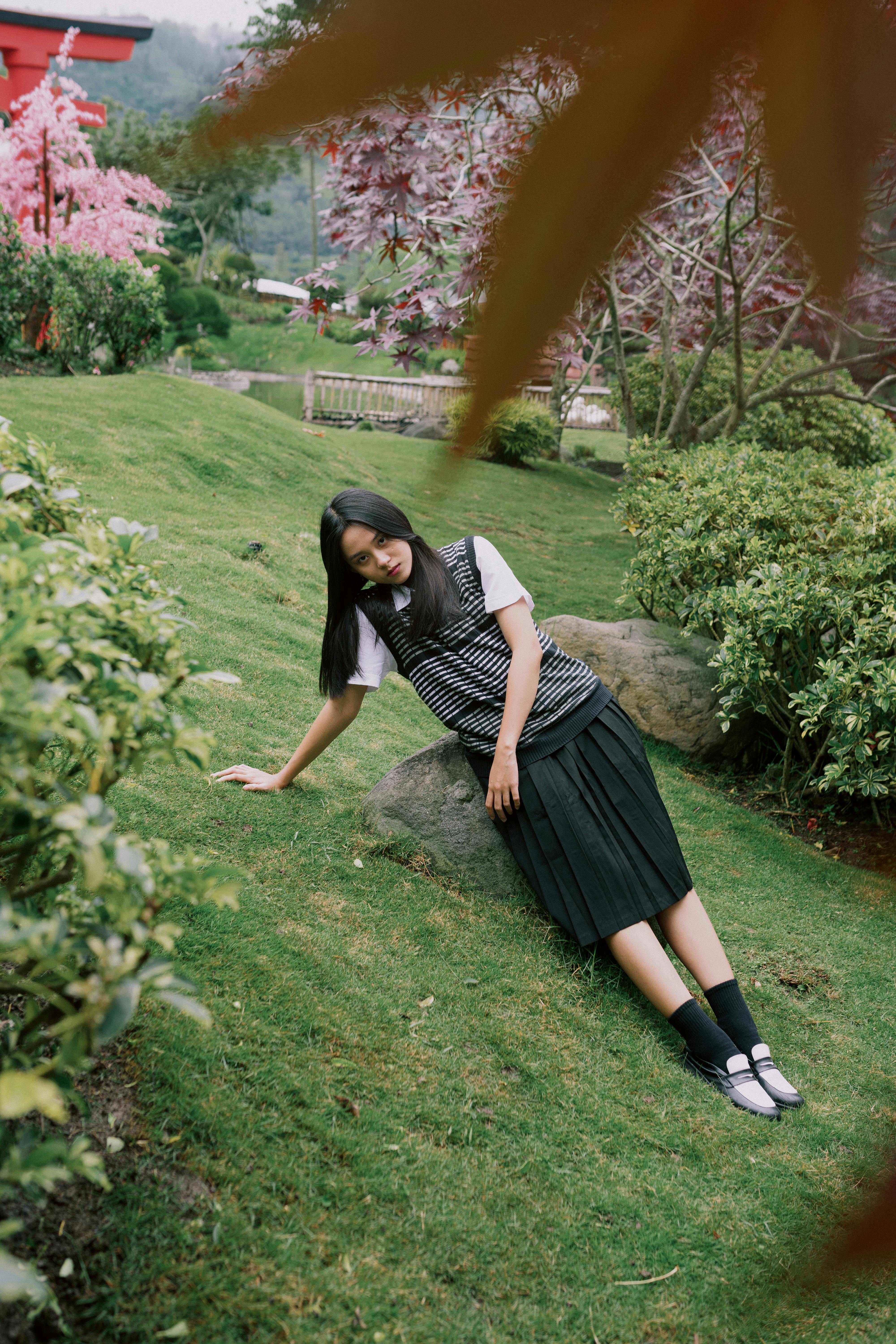 Ilmainen Nainen puutarhamiljöössä, rehevän vihreyden ja vaaleanpunaisten kukkien ympäröimänä, nauttii rauhallisesta ympäristöstä. Kuvapankkikuva