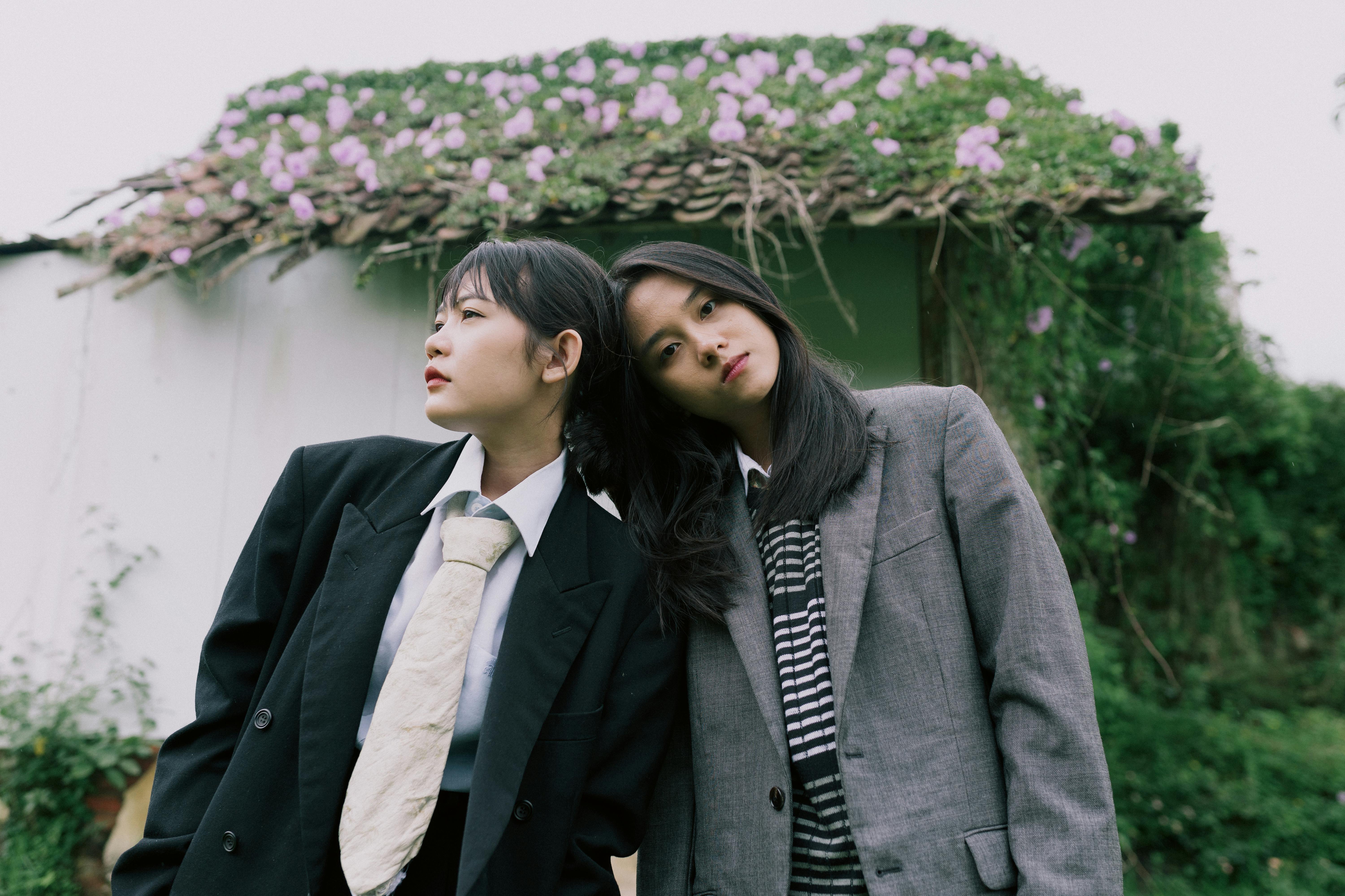 Ilmainen Muodikkaita nuoria naisia ​​puvuissa maalaismaisen kukkaisen taustan edessä ulkona. Kuvapankkikuva