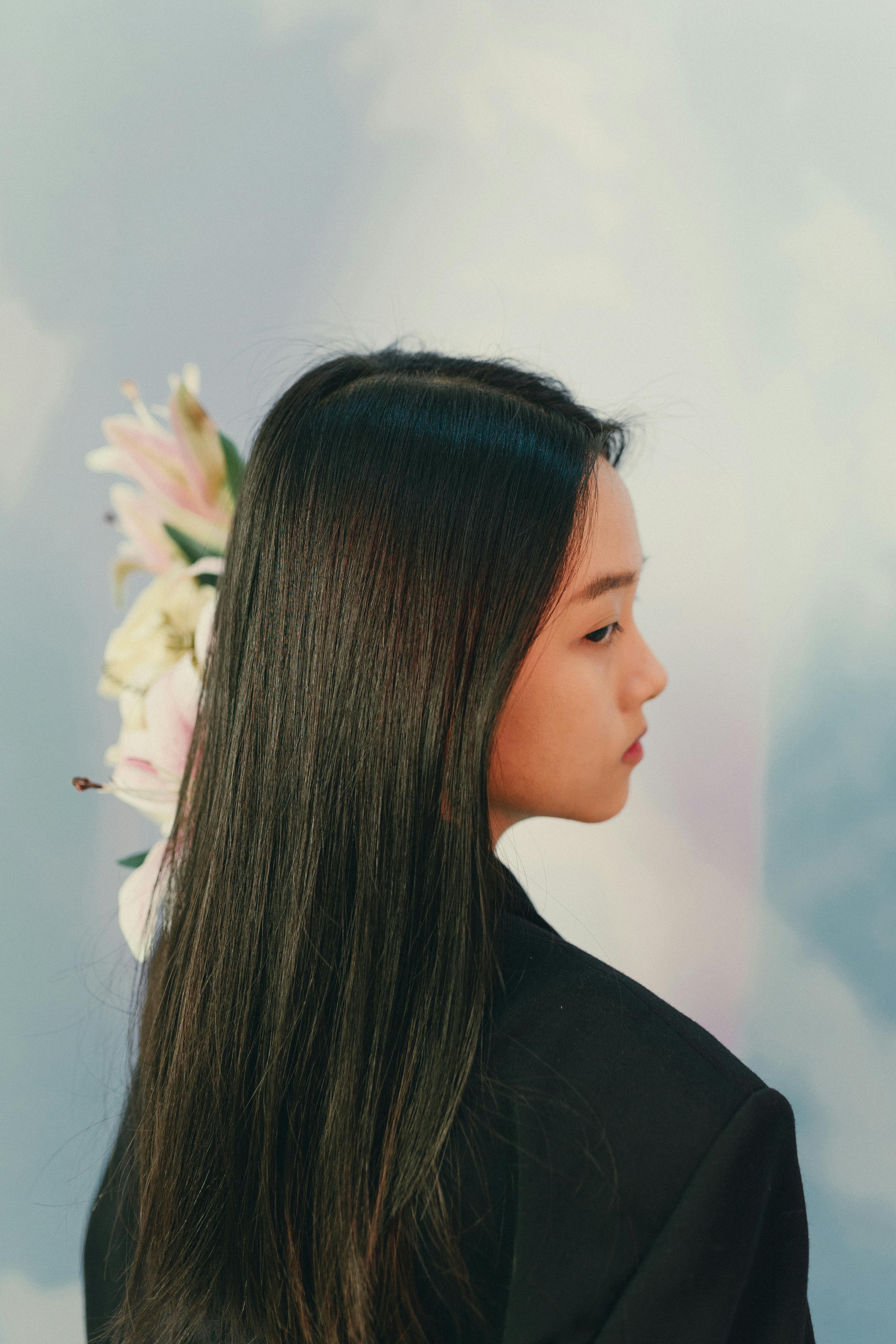 Free Beautiful side profile of a woman in a black jacket with floral background. Stock Photo