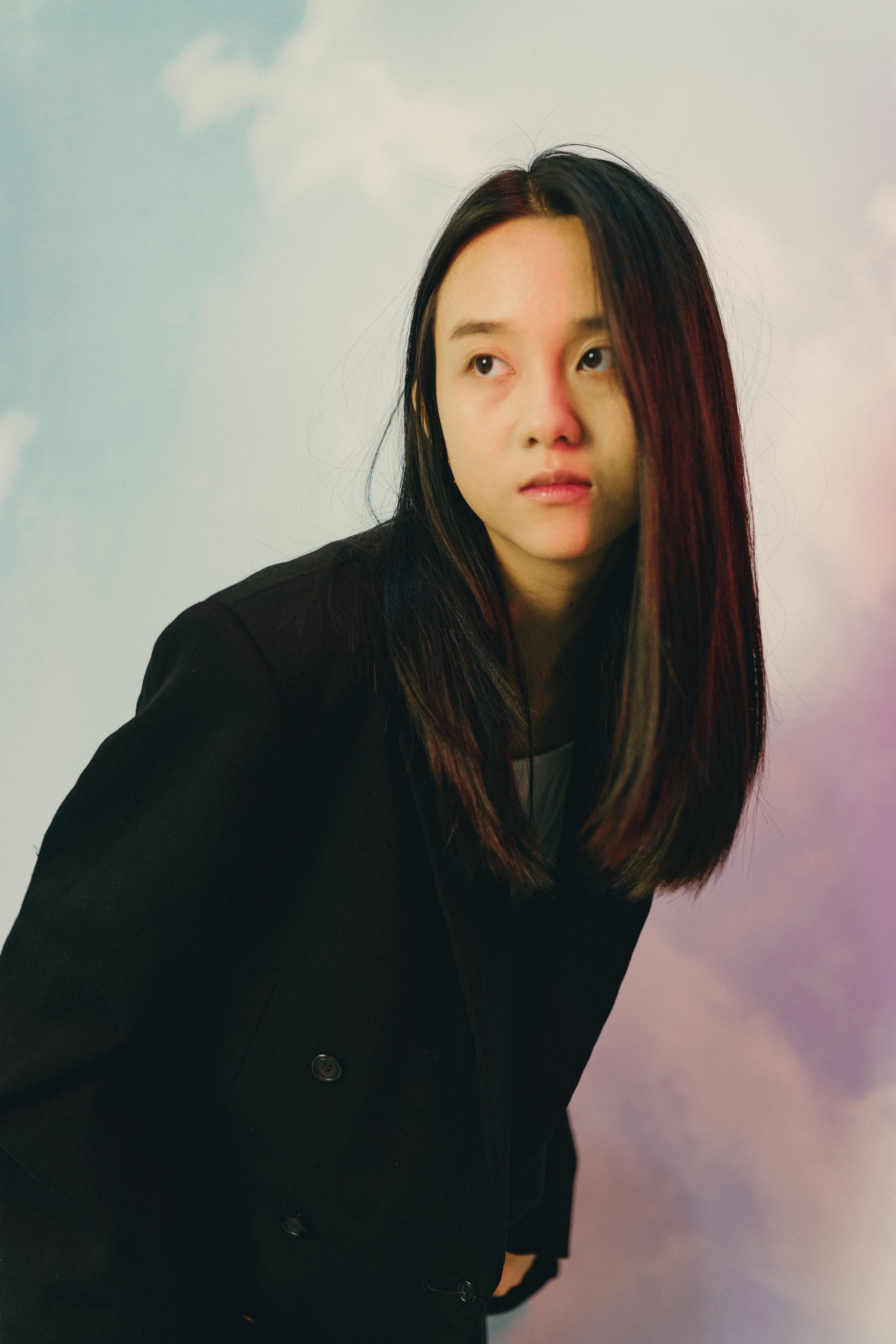 Stylish portrait of a young woman in a black jacket with a pastel sky background.