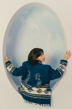 A woman in a blue patterned jacket poses against a sky-themed backdrop, creating a dreamy artistic effect.