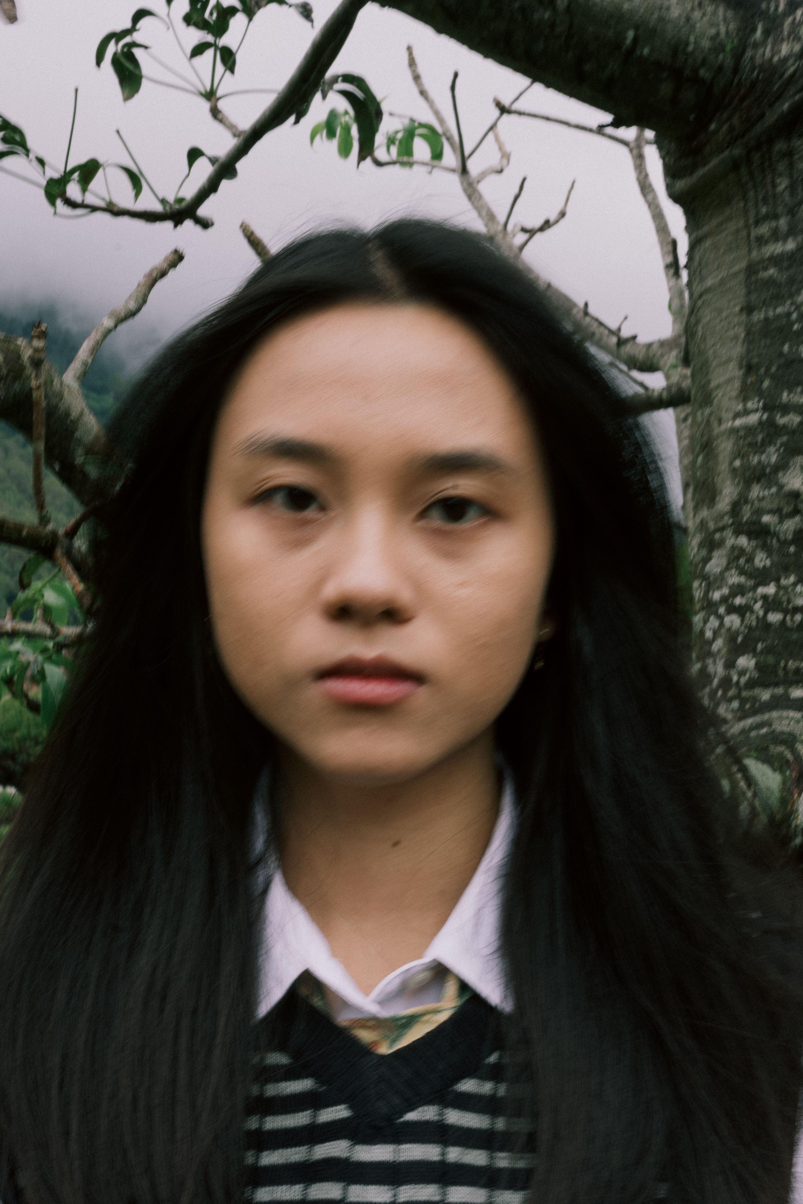 A blurred portrait of a young woman outdoors with natural background.