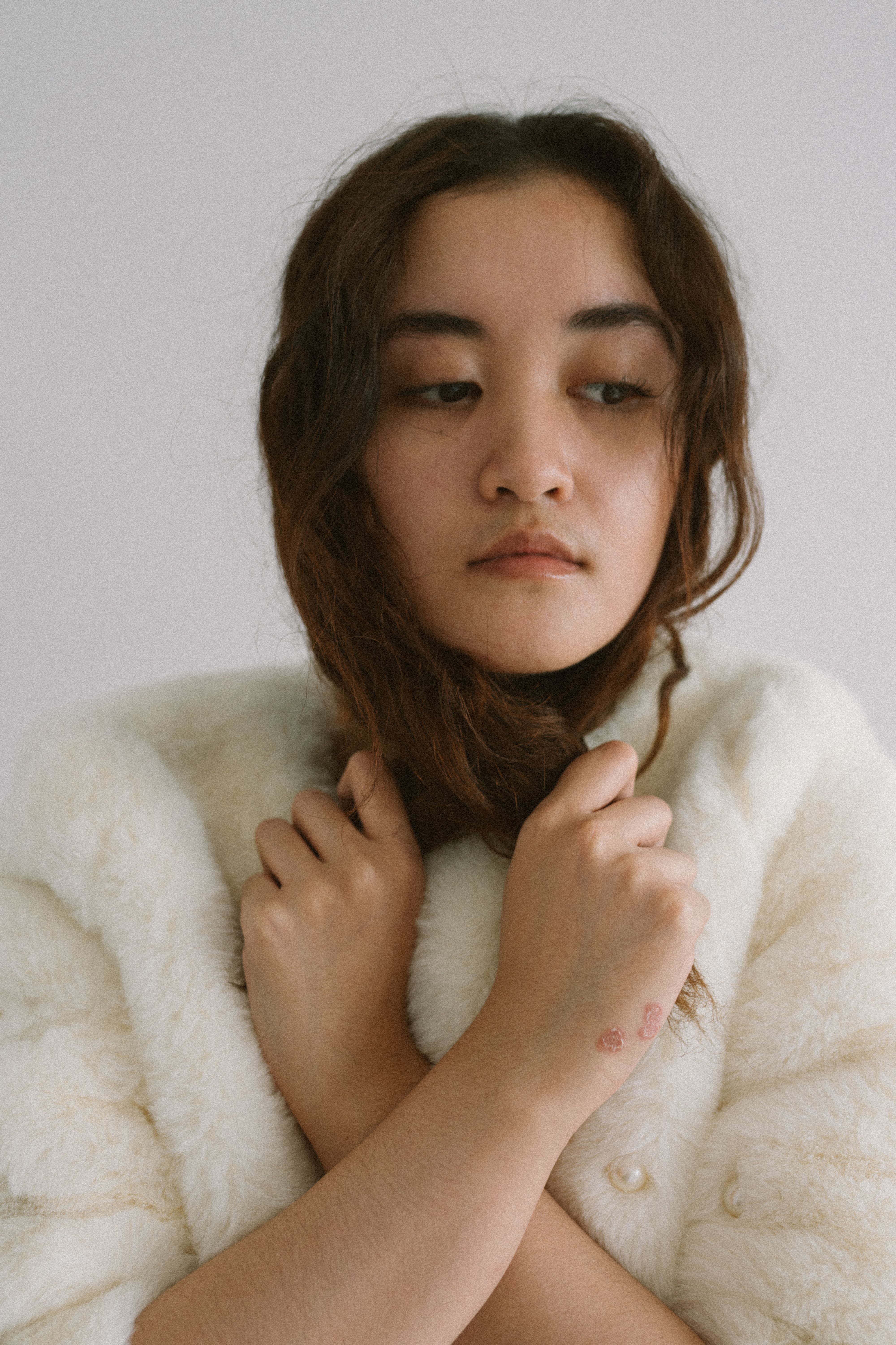 A thoughtful woman in a white fur coat stands indoors, creating a serene and introspective atmosphere.
