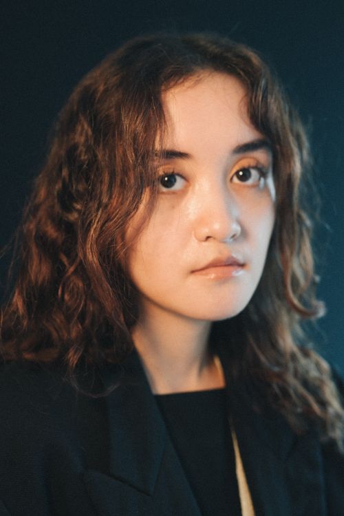 Free Close-up portrait of a young woman with curly hair against a dark background, showcasing her calm expression. Stock Photo