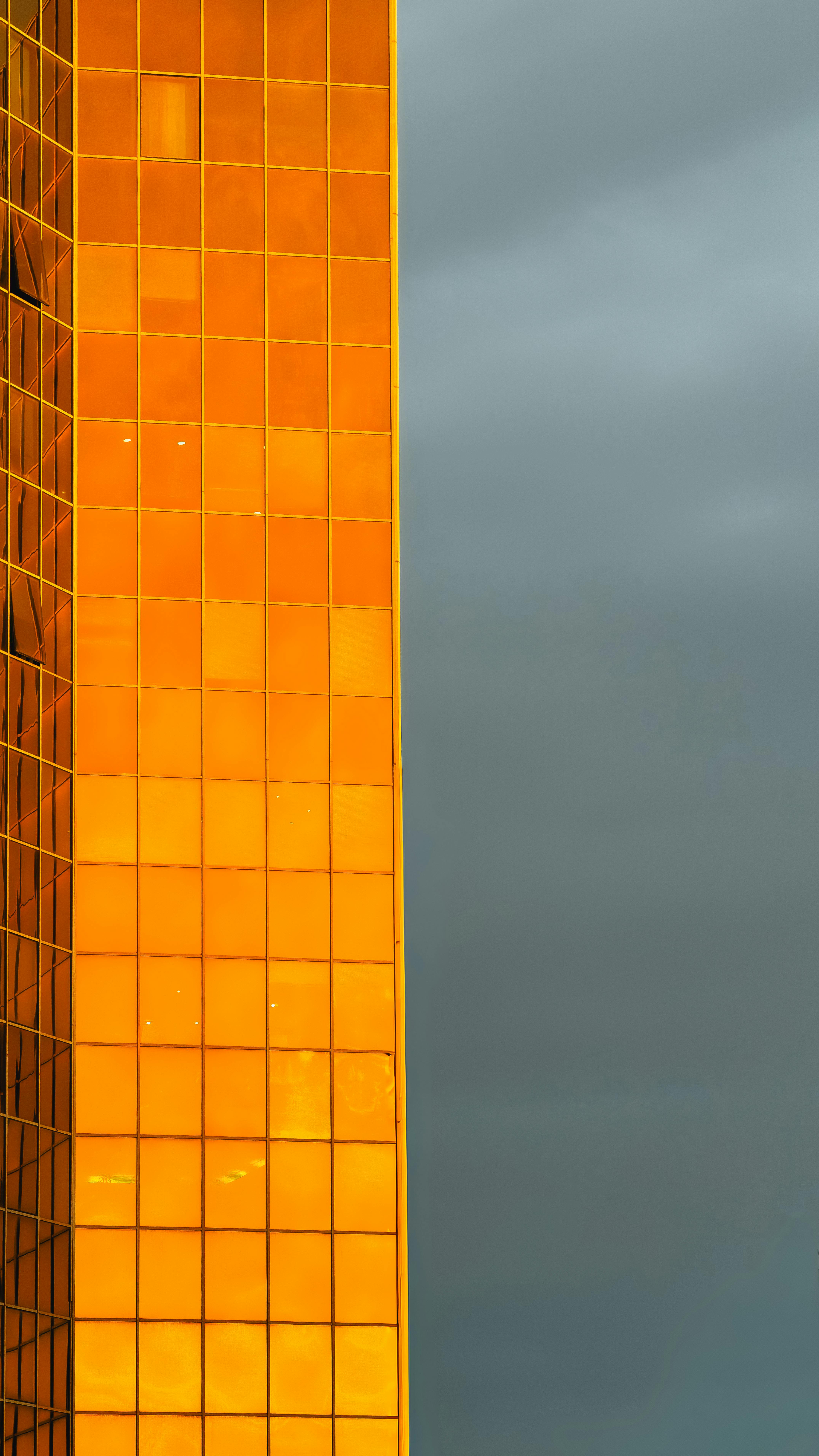 Kostenlos Eine eindrucksvolle Aufnahme einer goldenen Glasfassade, die sich vom stürmischen grauen Himmel abhebt. Stock-Foto