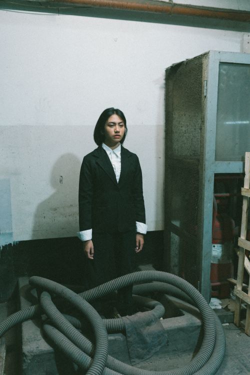 Free Woman in a suit standing in an industrial setting with pipes and machinery. Stock Photo