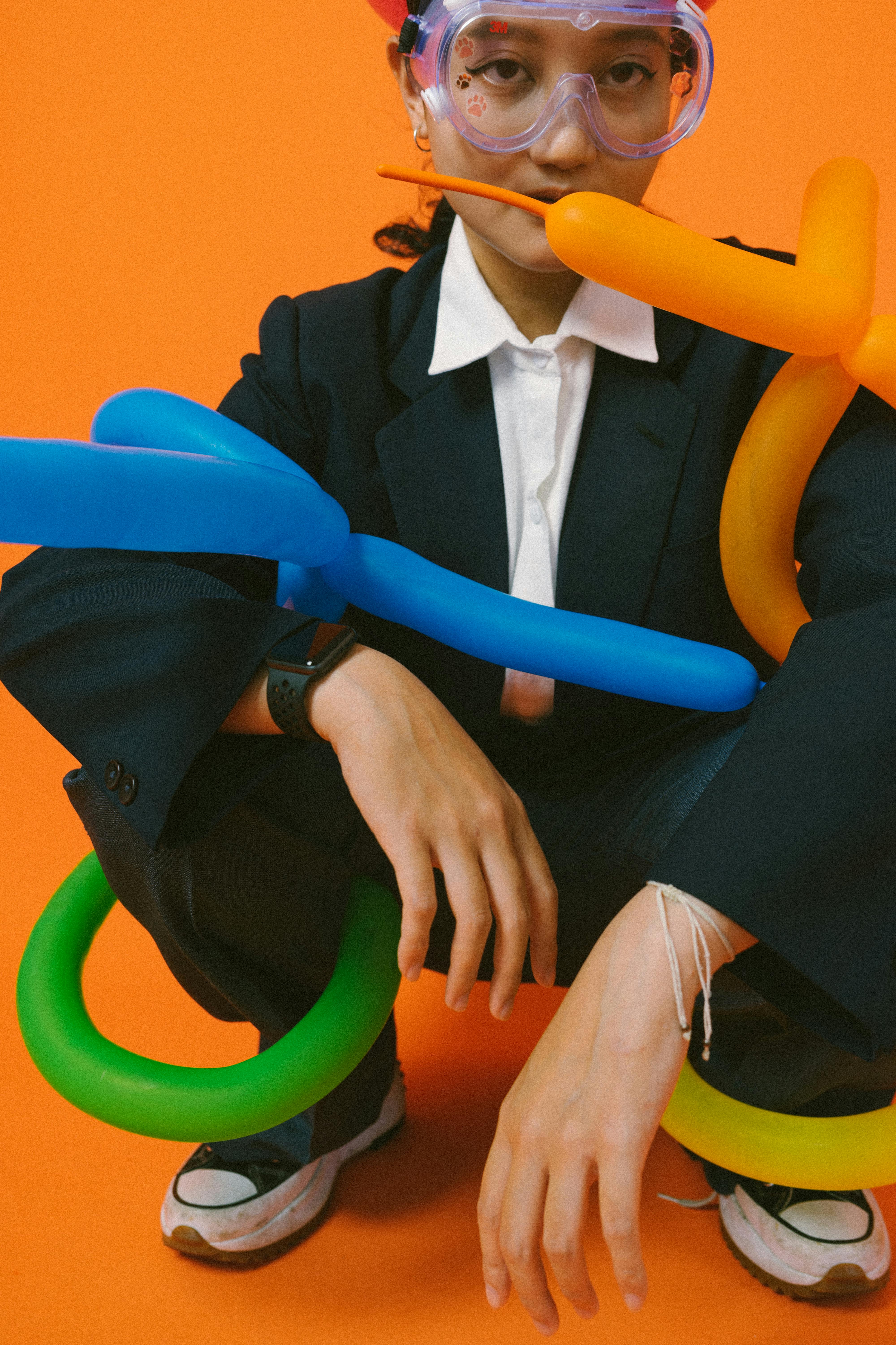 gratis Een persoon in een pak met ballonnen en een bril tegen een feloranje achtergrond. Stockfoto