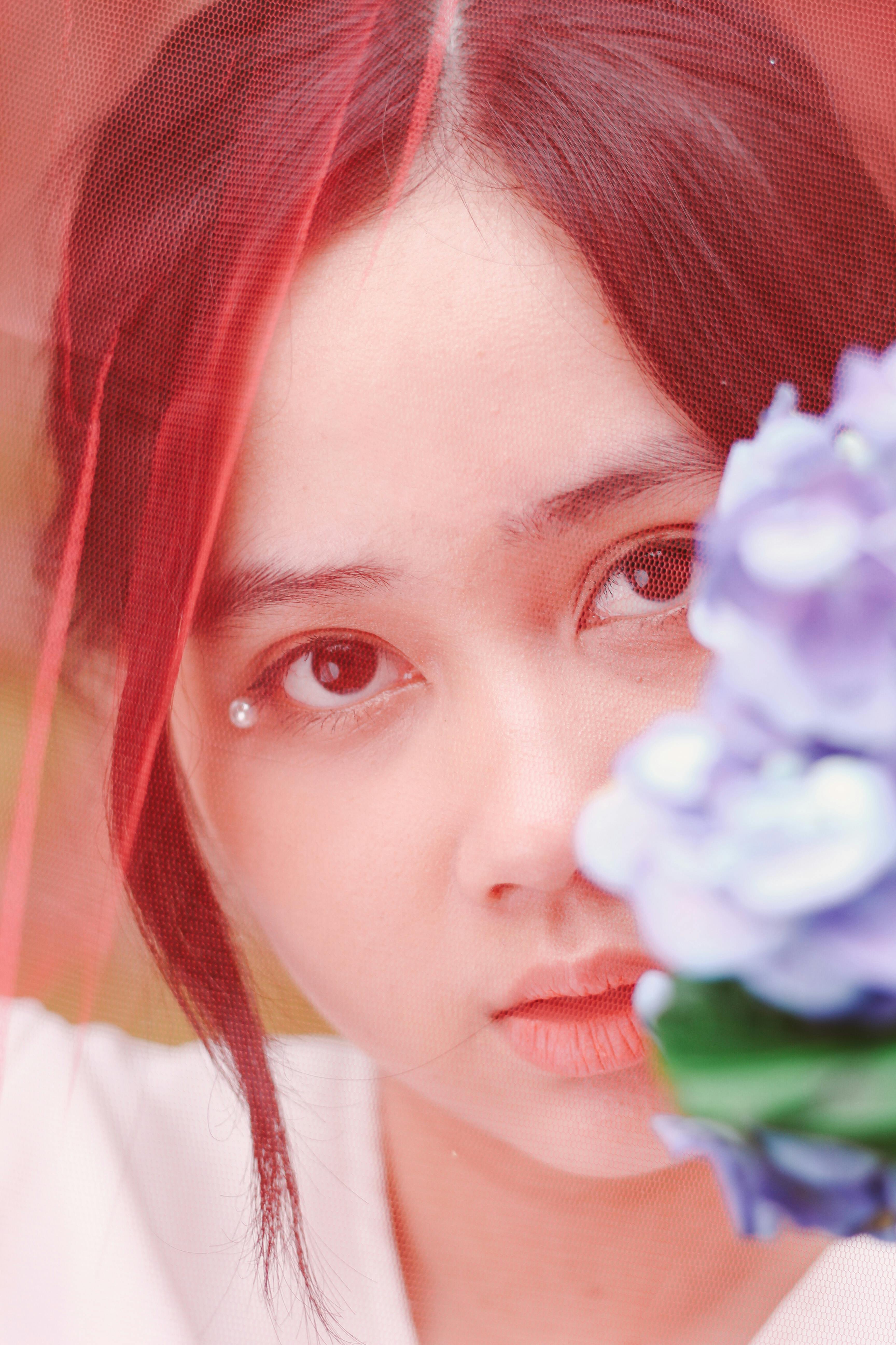 Bezpłatne Artystyczny portret młodej kobiety z niebieskimi kwiatami i czerwonym welonem, tworzący miękki i marzycielski efekt. Zdjęcie z galerii