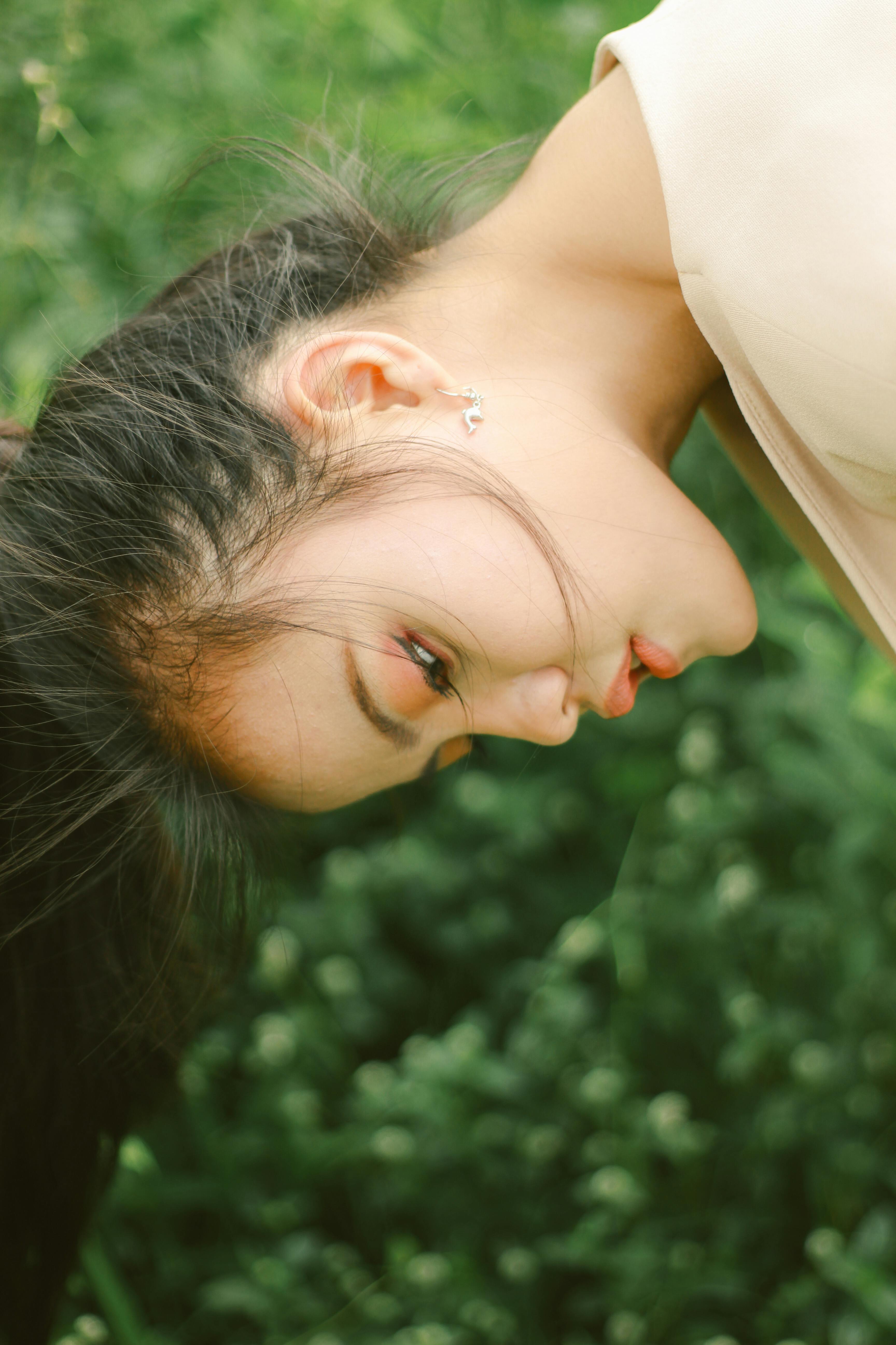 免费 一位年轻女子倚靠在郁郁葱葱的绿色环境中，神态宁静而沉思。 素材图片
