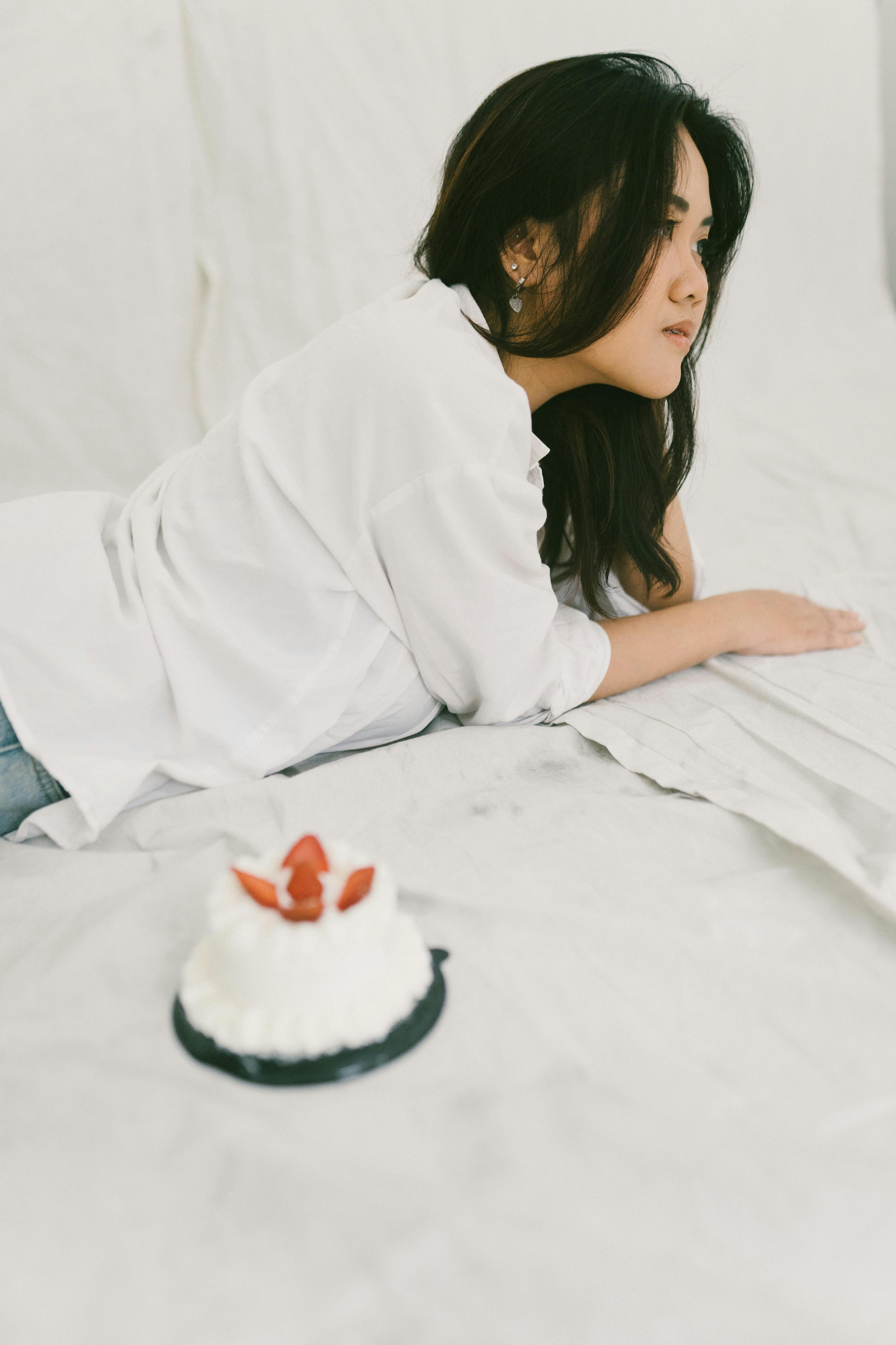 Miễn phí Một người phụ nữ nằm trên giường với món tráng miệng dâu tây, thể hiện tâm trạng thư thái và trầm tư. Ảnh lưu trữ