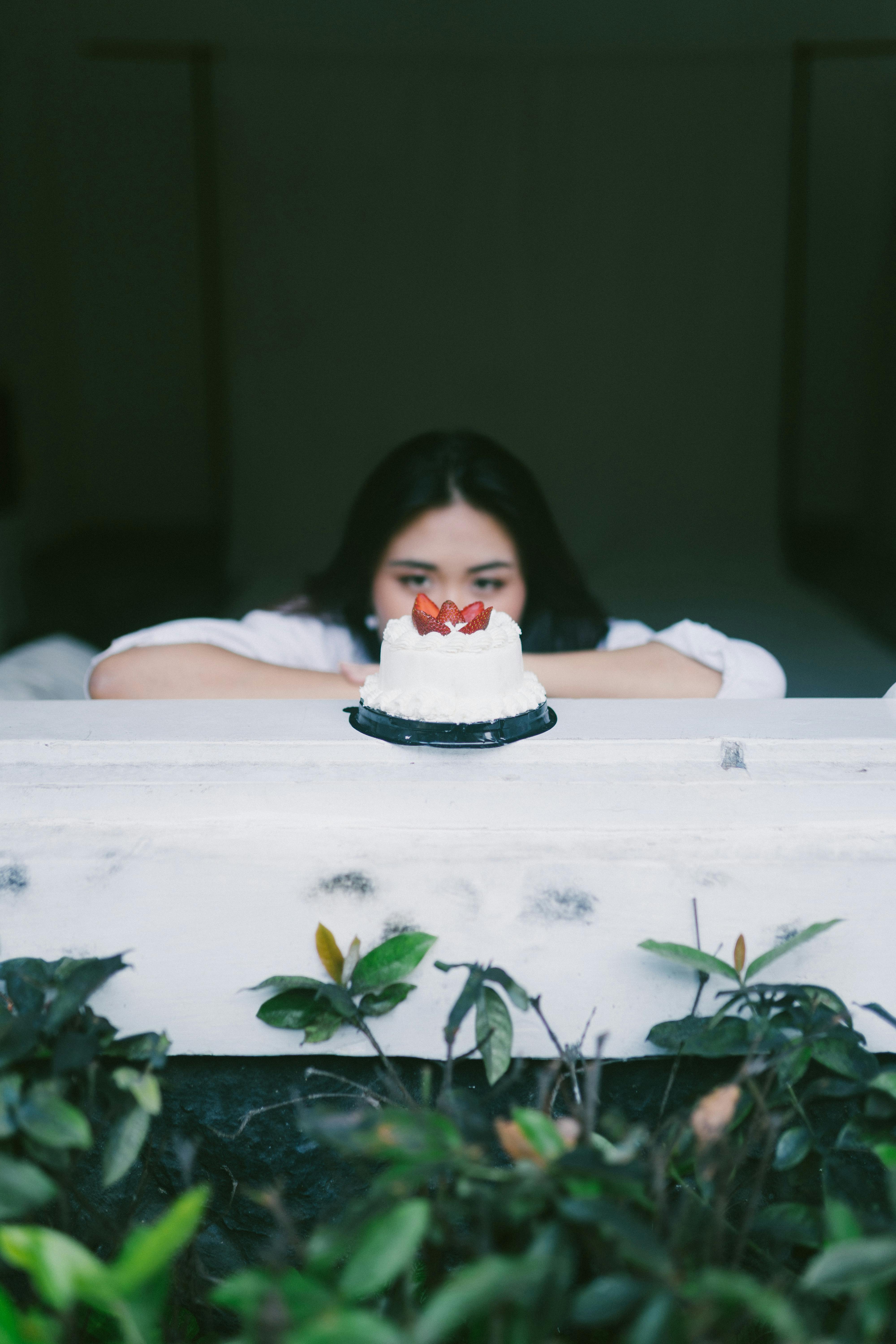 bezplatná Žena se dívá na jahodový dort na balkónové římse s listnatými rostlinami pod ním. Základová fotografie