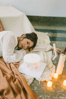 A serene indoor scene of a young woman resting with a cake and candles around her.