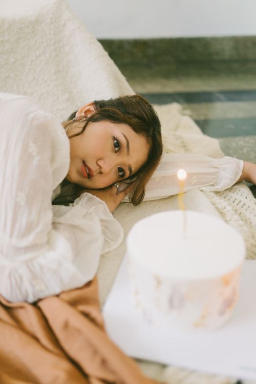 Free A young woman lying indoors beside a white birthday cake with a lit candle. Stock Photo