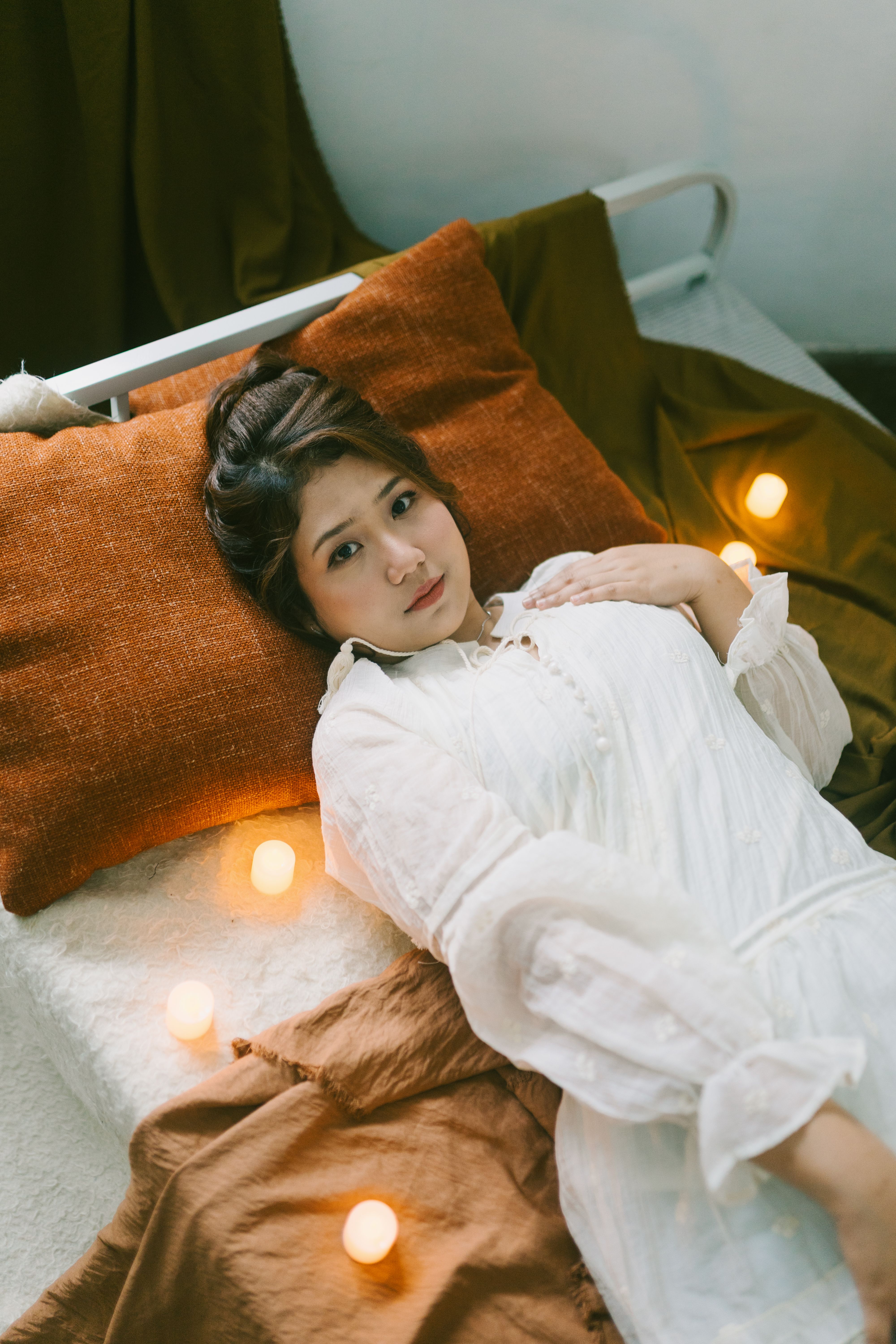 Woman in white dress relaxing on bed surrounded by soft ambient lights, creating a tranquil mood.