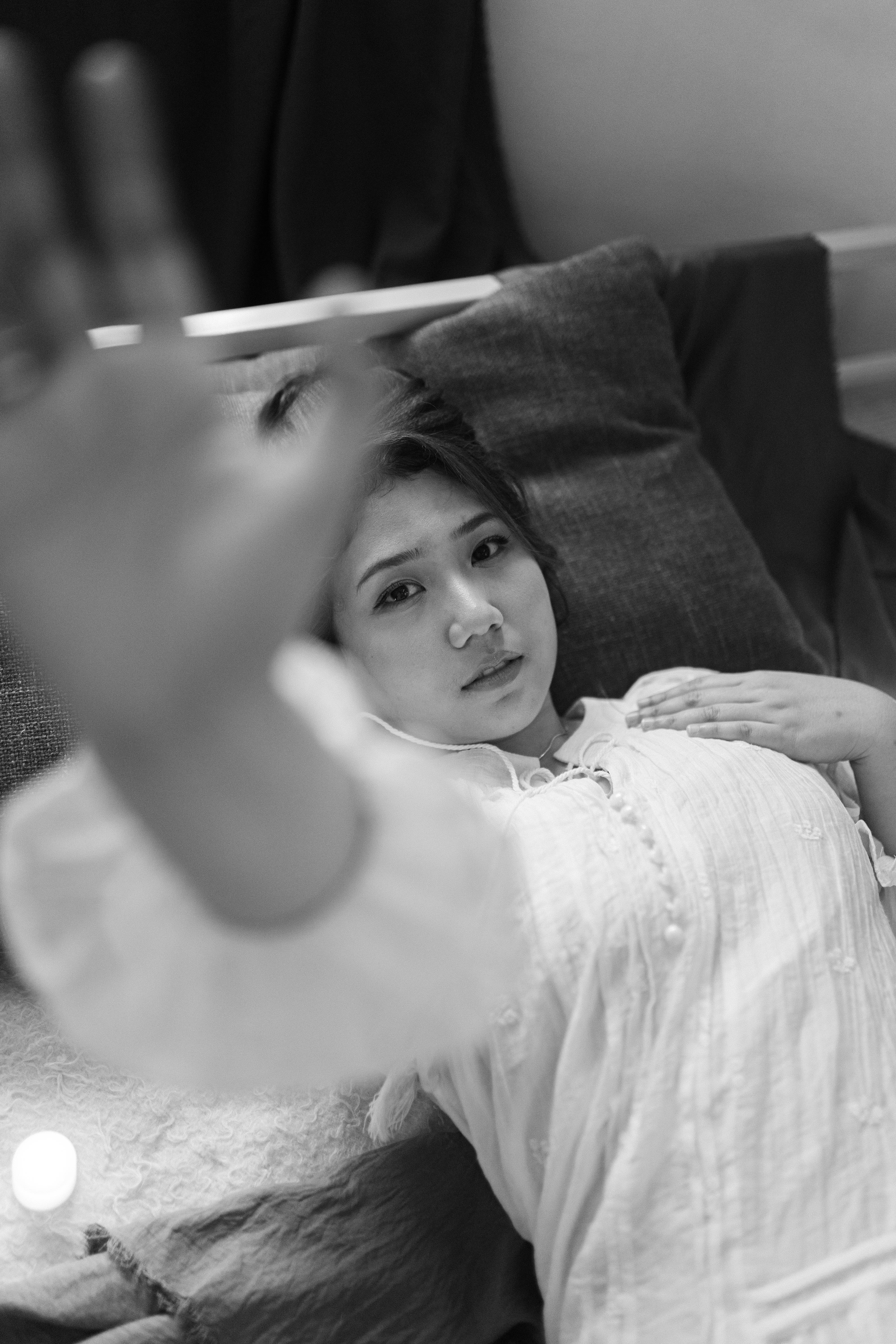 Free A serene black and white portrait of a woman lying on a sofa, reaching towards the camera. Stock Photo