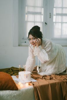 Smiling woman indoors by cake and candles, enjoying a birthday celebration.