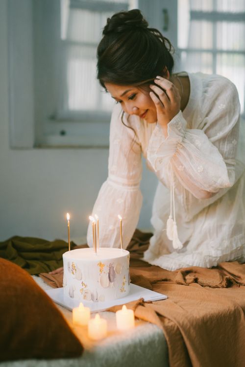 Free A young woman in a white dress celebrates her birthday indoors with lit candles and a cake. Stock Photo