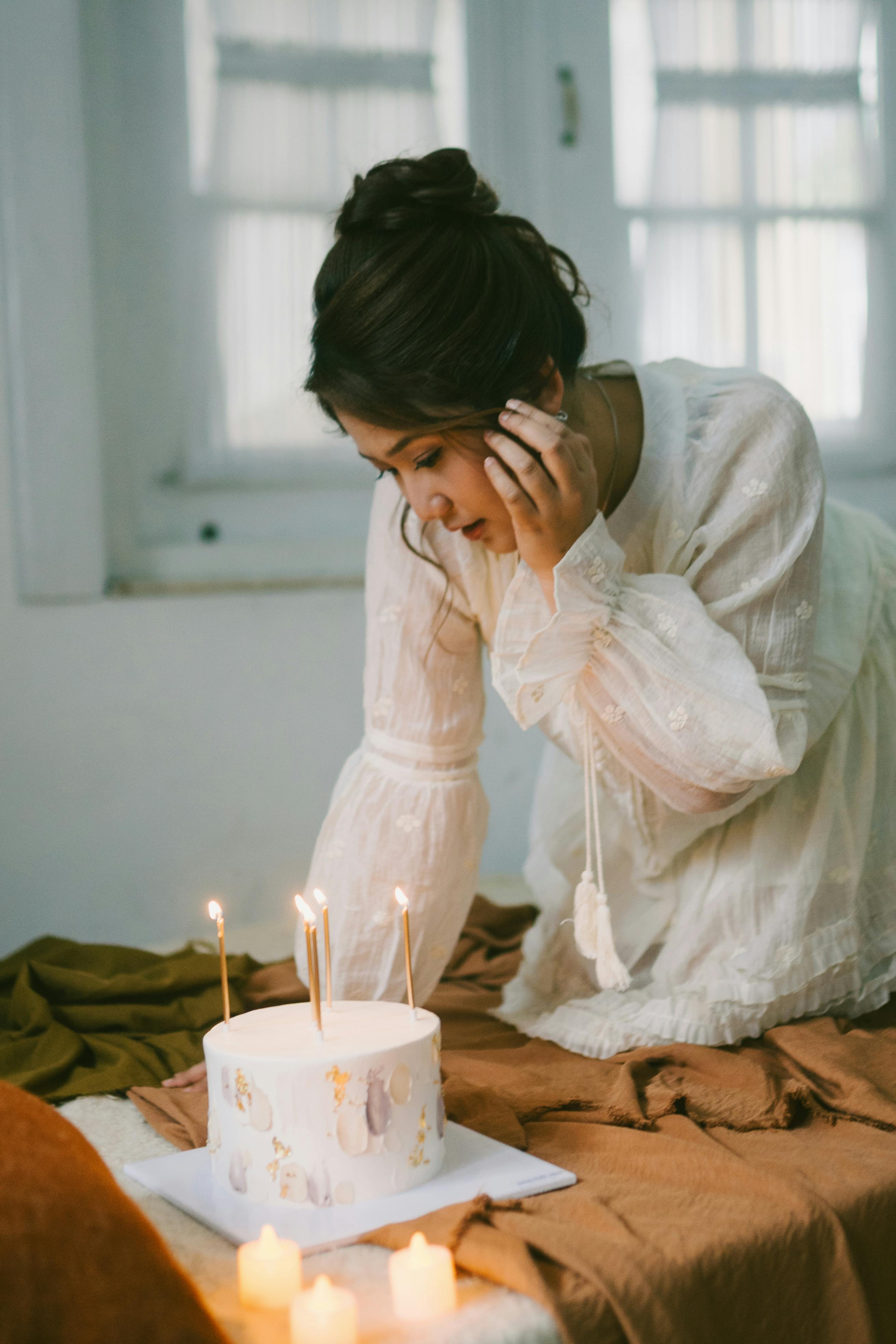 Miễn phí Một cô gái trẻ mặc váy trắng cúi xuống chiếc bánh sinh nhật có nến trong một khung cảnh ấm cúng. Ảnh lưu trữ