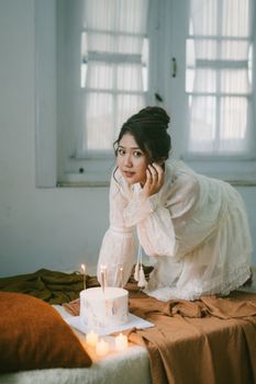 A young woman in a white dress celebrates with a birthday cake and candles indoors.