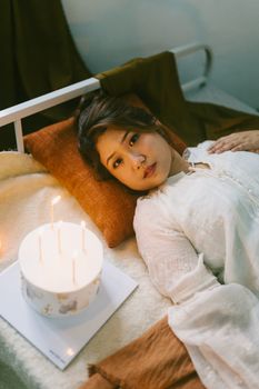 Young woman relaxing in soft lighting with a candle-lit atmosphere, creating a tranquil mood.