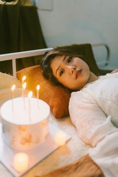 A woman relaxing in a cozy room with a candlelit cake, exuding warmth and tranquility.