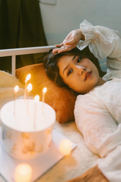 Free A relaxed woman lies beside a candlelit cake on a bed, creating a warm and cozy atmosphere. Stock Photo