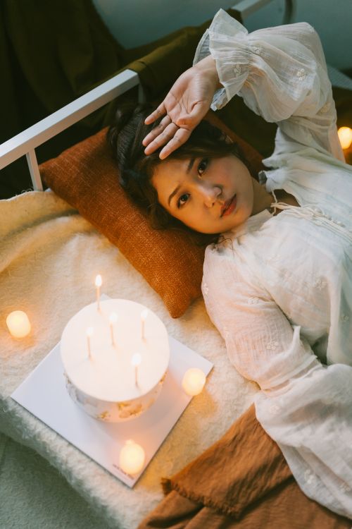 Free Woman in white blouse resting beside a cake and candles, creating a serene and cozy atmosphere. Stock Photo