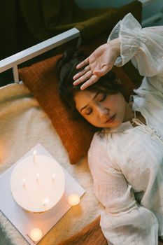 Woman in serene setting with candles, laying peacefully. Warm, calming atmosphere indoors.