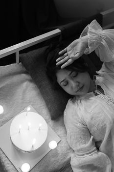 Black and white photo of a woman resting in bed next to a candle-lit cake, creating a serene atmosphere.