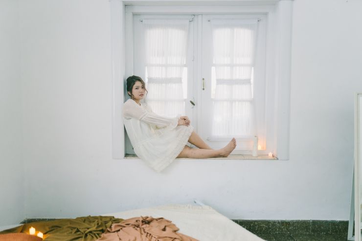A woman seated in a window nook of a bedroom — photo by Rizky Sabriansyah on Pexels