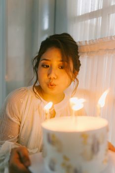 A young woman making a birthday wish as she blows out candles on a cake indoors.