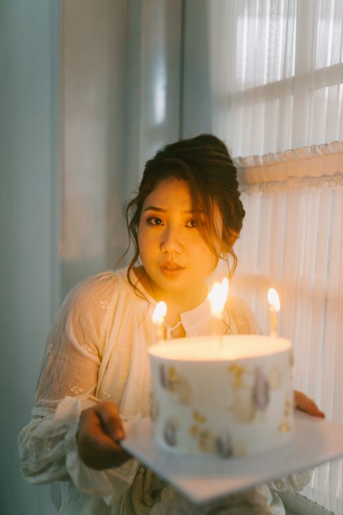 Free A young woman in a soft-lit room, holding a lit birthday cake. Stock Photo