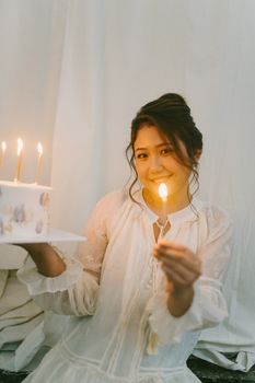 Cheerful woman holding a lit candle and cake for her birthday celebration indoors.
