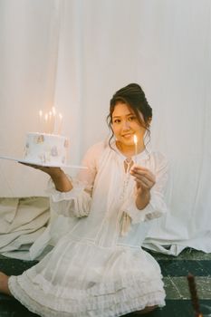 Young woman sitting indoors holding a birthday cake with lit candles, celebrating a birthday.