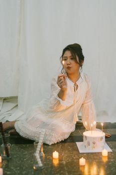 Woman in white dress celebrating birthday with lit cake and candles.