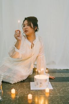 Young woman in white dress lighting birthday cake candles, creating a warm, festive ambiance.