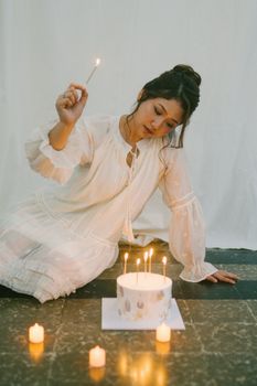 Elegant woman lighting candles on a birthday cake indoors, creating a warm and intimate atmosphere.